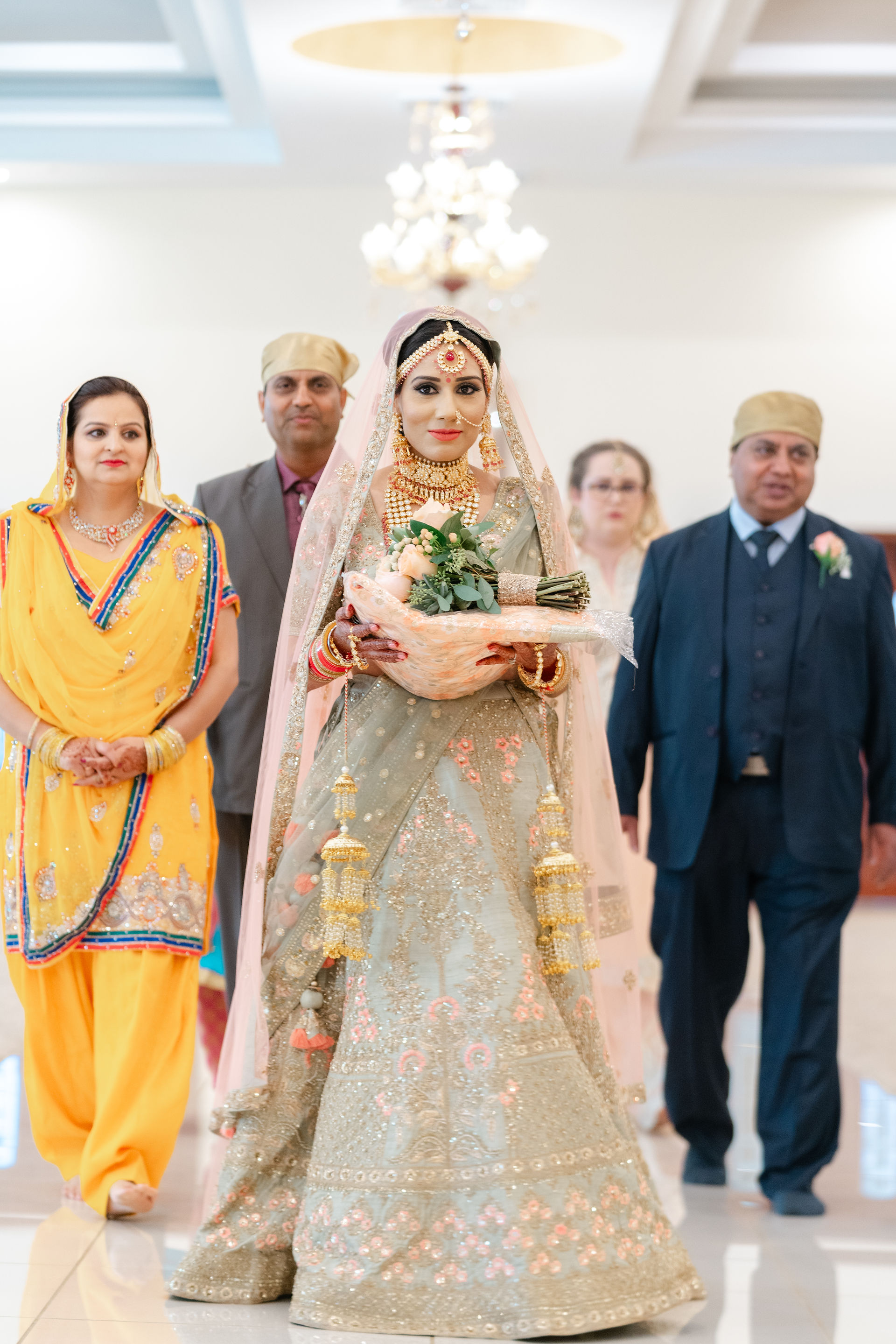 A South Asian bride in a traditional gold lehenga being escorted by her family into the Sacramento Gurdwara for her Sikh wedding ceremony.