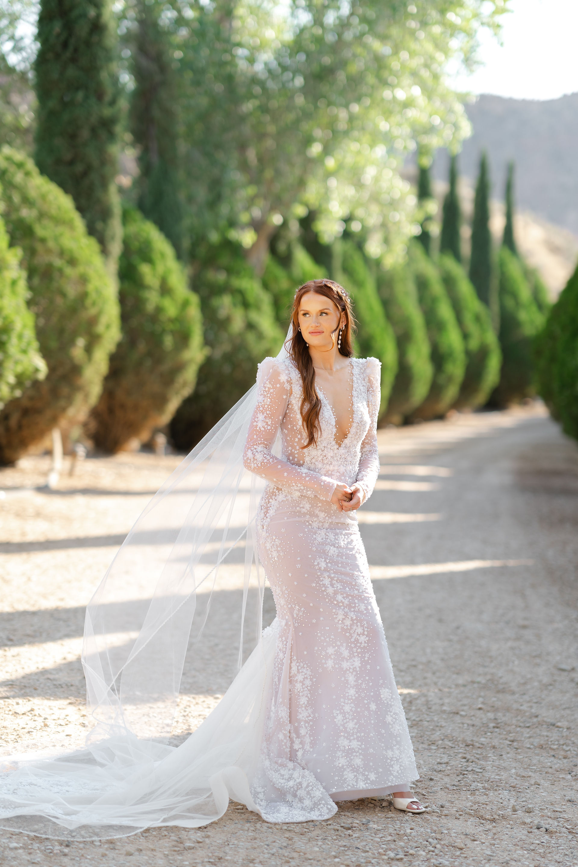 The bride, Laurel, posing in her stunning long-sleeved lace gown on a scenic tree-lined path during her Zion National Park Wedding.