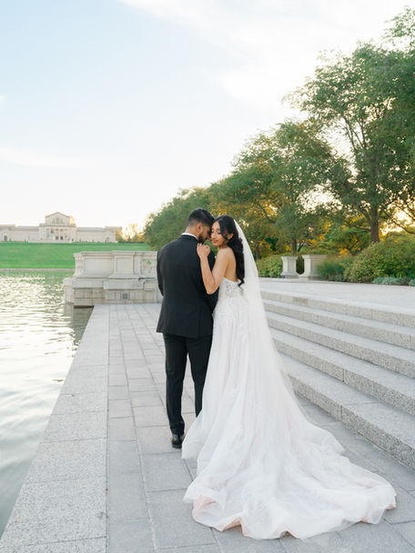 A couple standing on a stone pier by a lake, captured in a wide shot that emphasizes the serene landscape.
