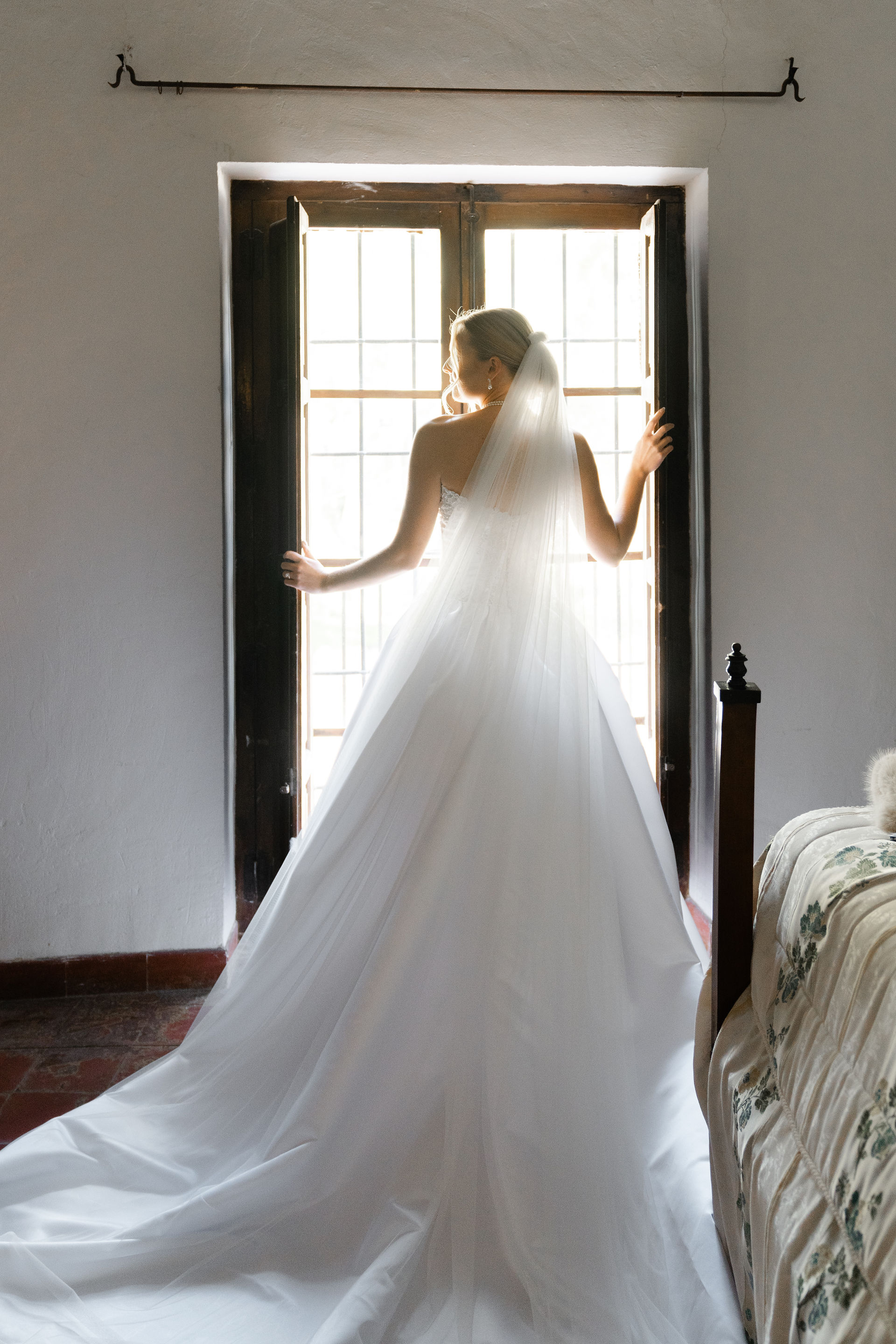 Artistic bridal portrait of a bride looking over her shoulder at a rustic Spanish villa window.