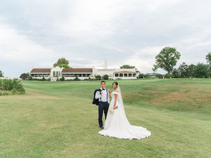 Wide-angle outdoor portrait of bride Sarah and groom Vince posing on the manicured green lawns of Norwood Hills Country Club in St. Louis, Missouri, featuring the historic white clubhouse in the background.