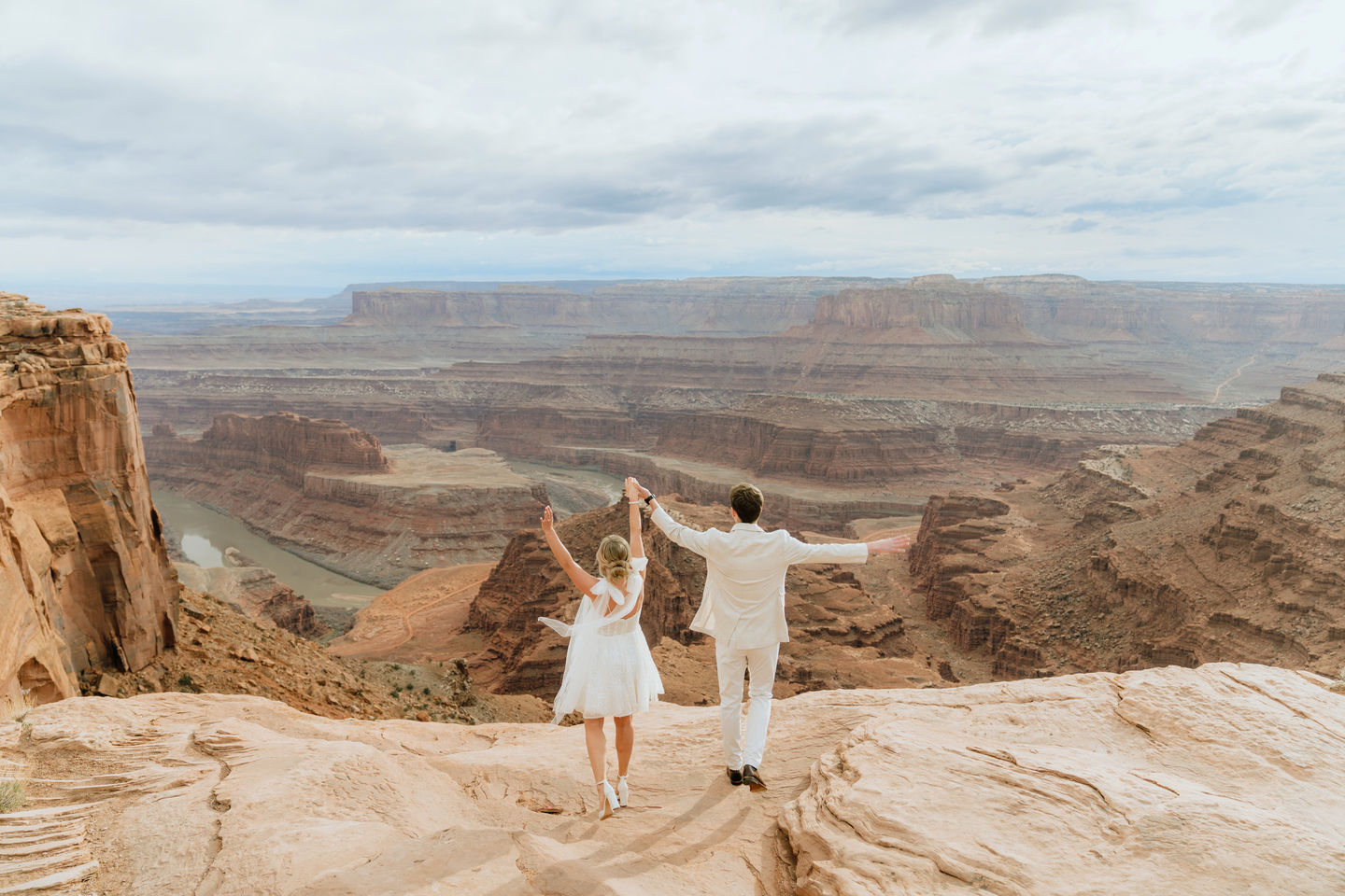 A bride and groom celebrating their destination elopement at Dead Horse Point State Park, standing on a high desert plateau overlooking the vast Colorado River canyon.