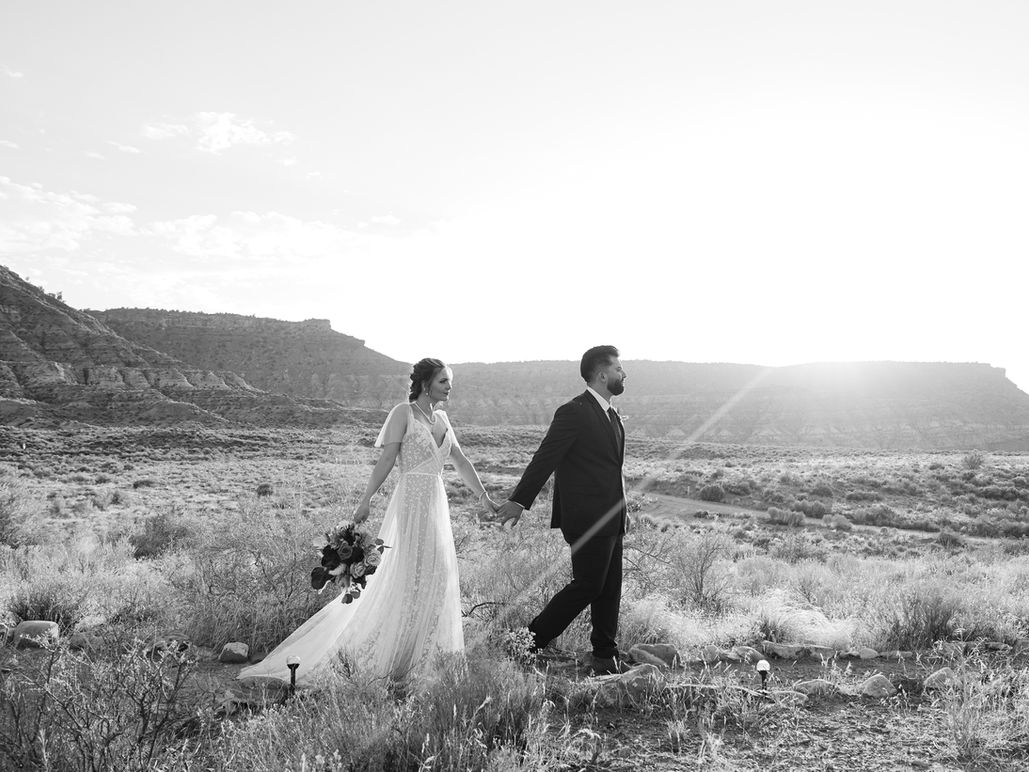 Black and white photo of a bride and groom walking hand-in-hand through a rugged mountain valley.