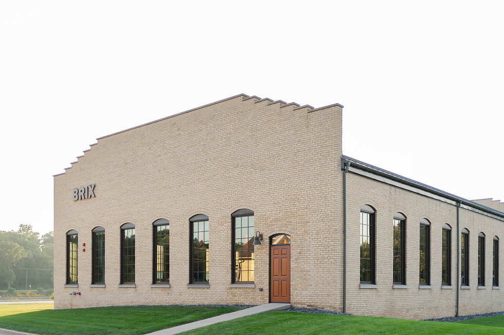 Brick building with arched windows and a brown door, labeled "BRIX." It stands on a grassy lawn against a clear sky.