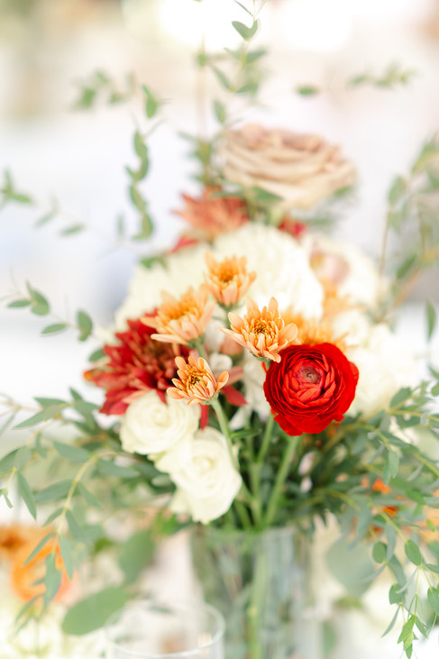 A vibrant floral centerpiece featuring white roses and orange ranunculus on a reception table at a Colorado Trading Post wedding.