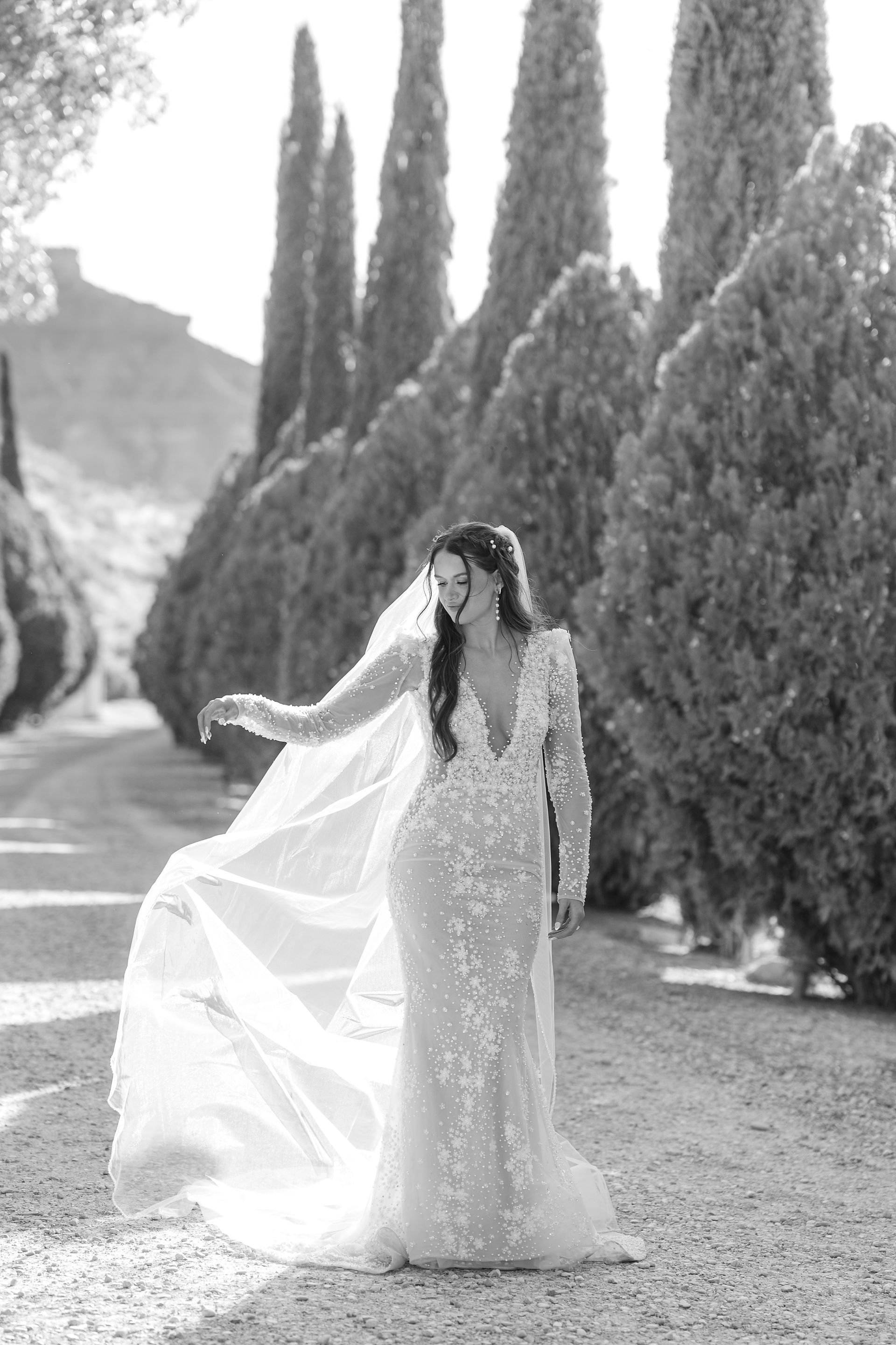 A full-length bridal portrait of Laurel standing amidst tall Mediterranean cypress trees, showcasing the elegance of her Zion National Park Wedding attire.