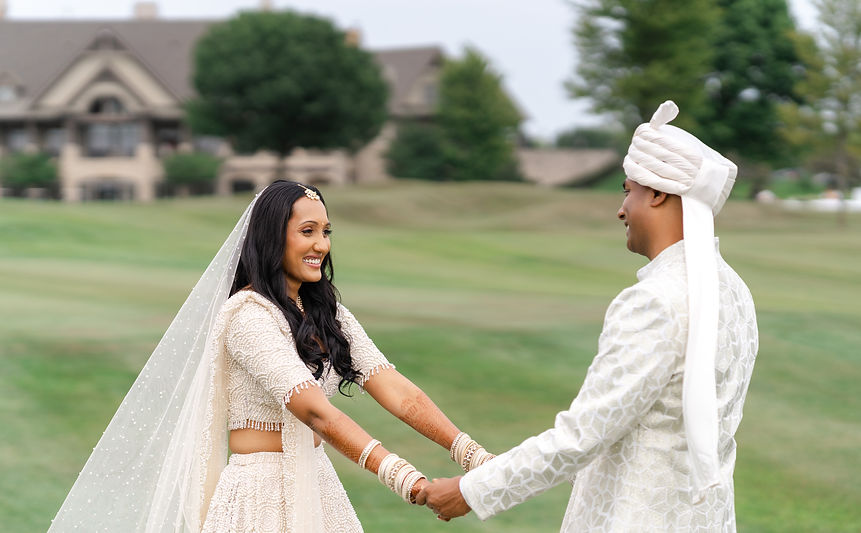 A South Asian bride and groom holding hands and smiling on the lush green course of the Bolingbrook Golf Club during their wedding portrait session.