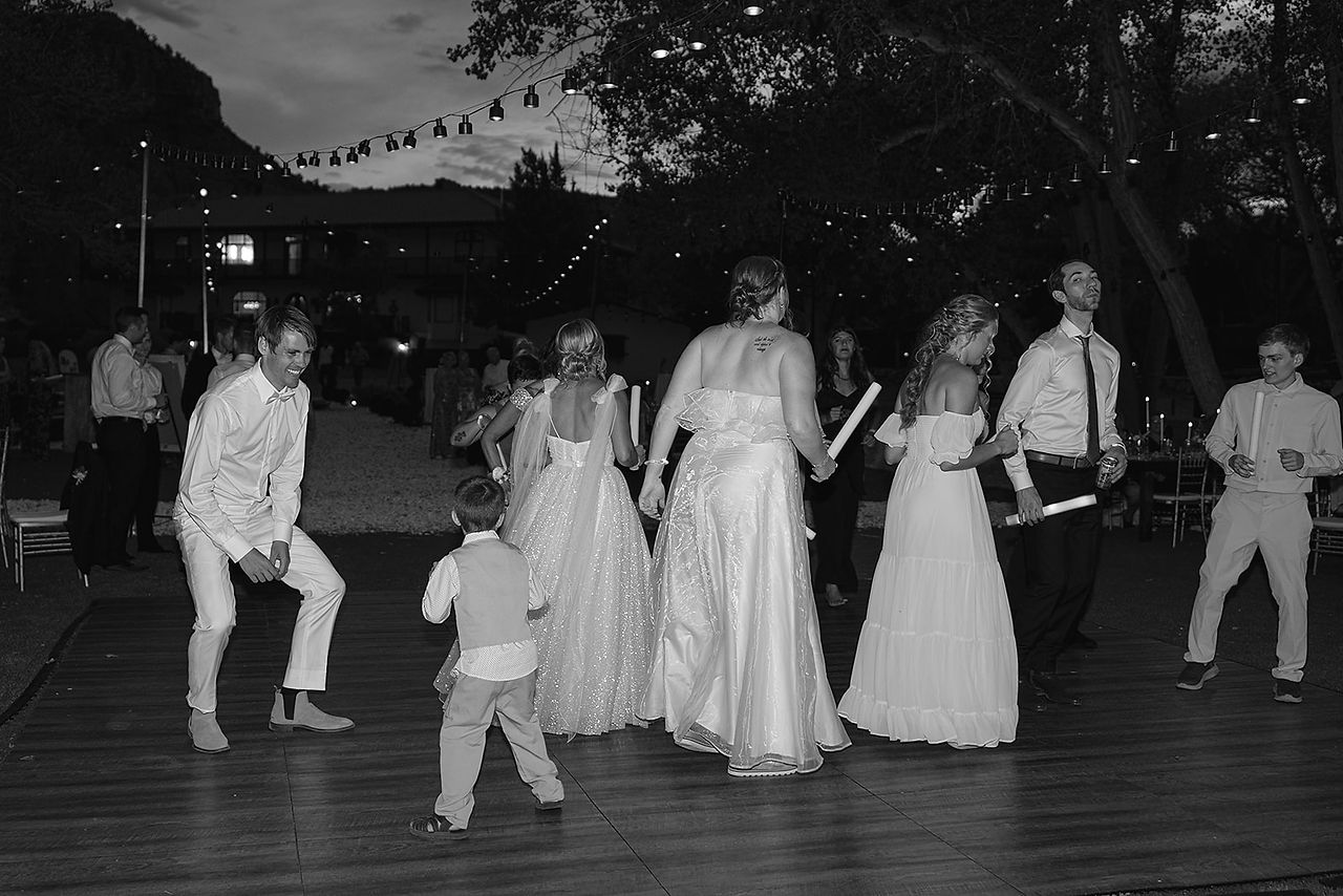 A wide shot of wedding guests celebrating with white glow sticks on a large outdoor dance floor at a Zion National Park wedding.