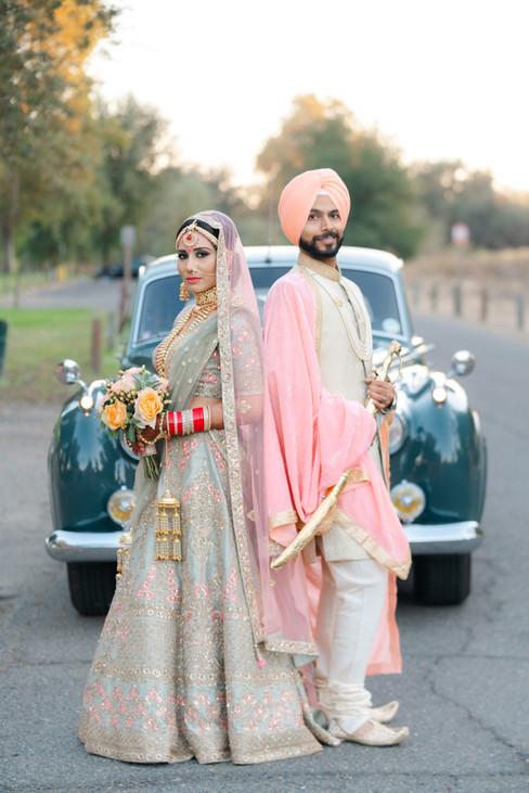 A stylish Sikh bride and groom posing in front of a vintage wedding car in Sacramento, blending old-world glamour with traditional Indian wedding fashion.