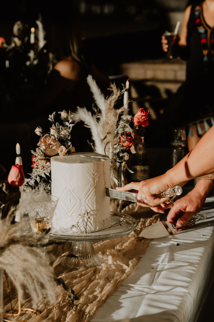 A detailed close-up of a three-tier white wedding cake decorated with delicate dried florals, set outdoors in a desert environment.