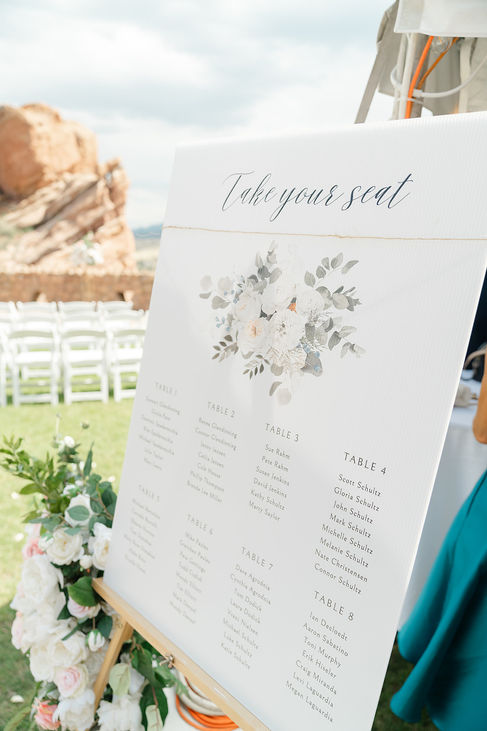Elegant wedding reception seating chart and white chairs at an outdoor Colorado Trading Post wedding ceremony.