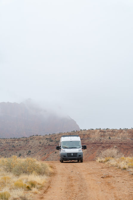 White adventure van driving down on a dirt road in a remote desert canyon.