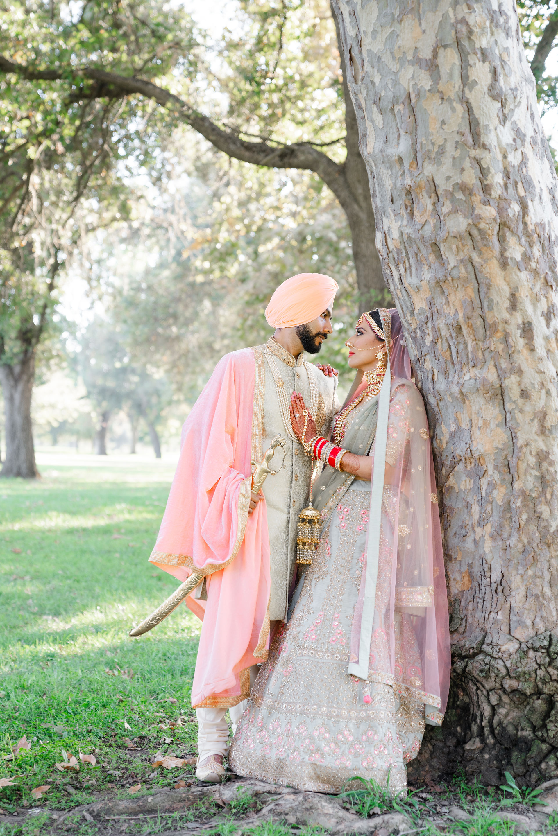A romantic full-length portrait of an Indian couple facing one another under a canopy of trees at a Sacramento wedding venue.