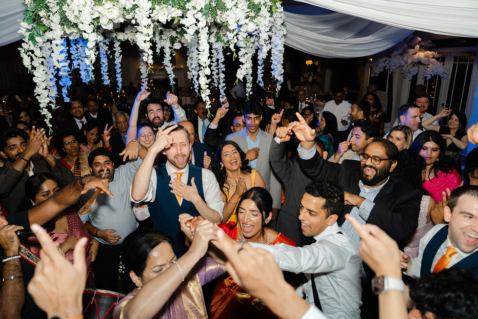 Vibrant shot of a crowded dance floor with guests cheering and dancing under hanging white floral decor during Sarah and Vince's St. Louis wedding reception.