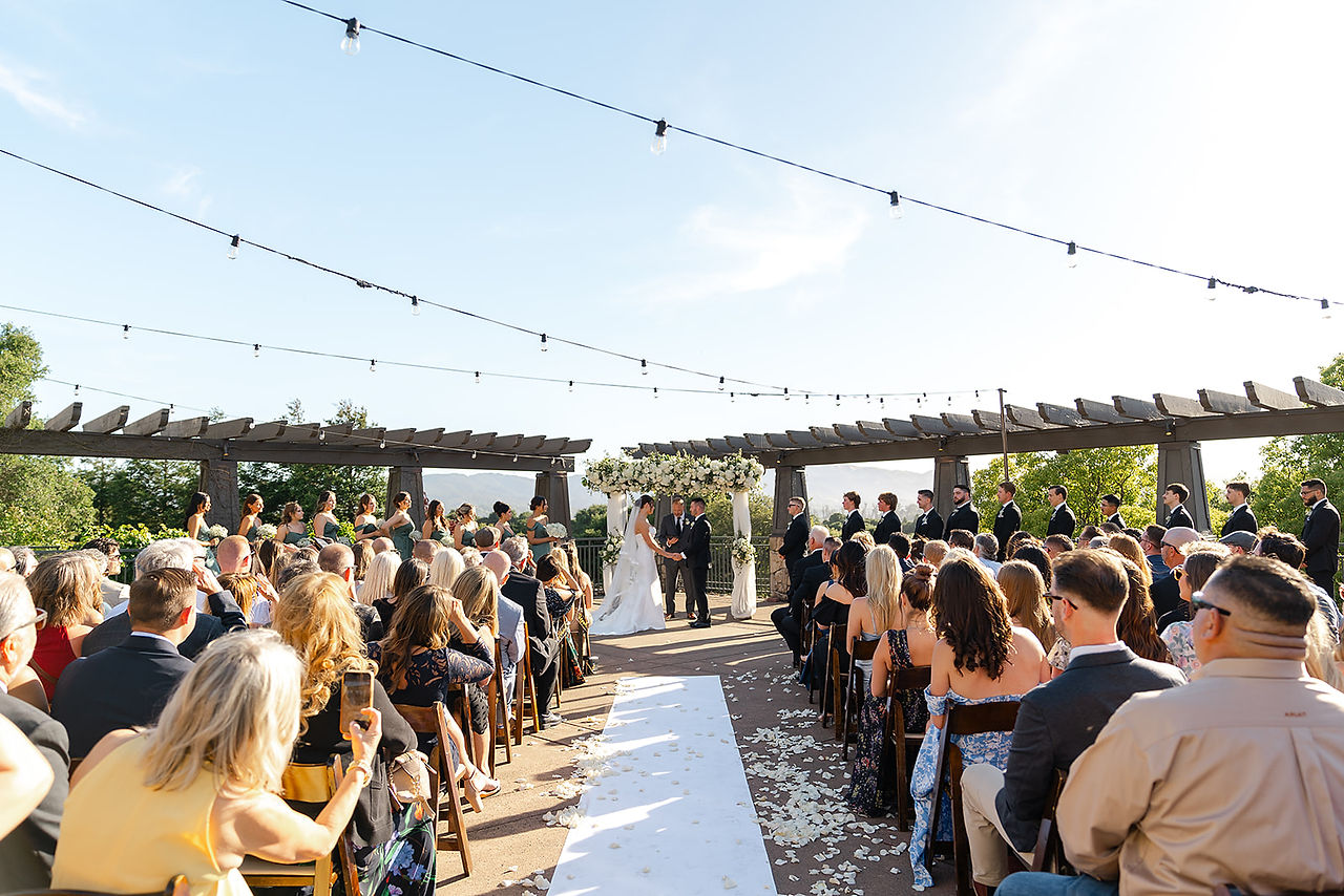 A scenic wide-angle view of the outdoor wedding ceremony at Stone Tree Golf Club in Novato, showing the couple at the altar surrounded by guests and rolling hills.