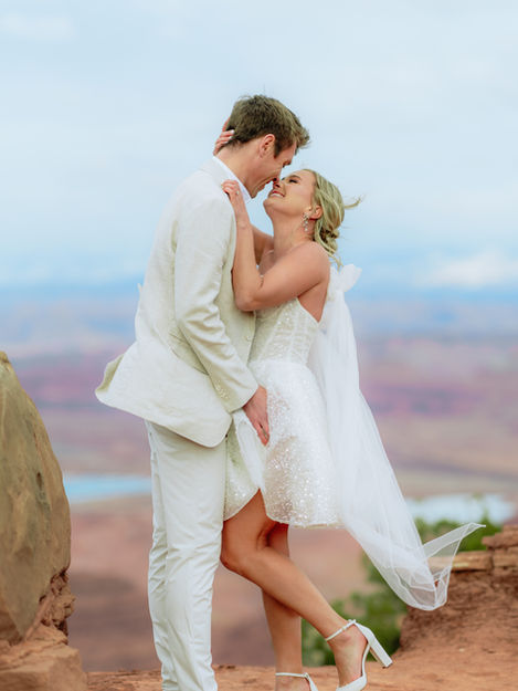 An adventurous bride and groom sharing an intimate embrace on a high desert plateau at Dead Horse Point State Park, overlooking the vast canyons of Moab, Utah.