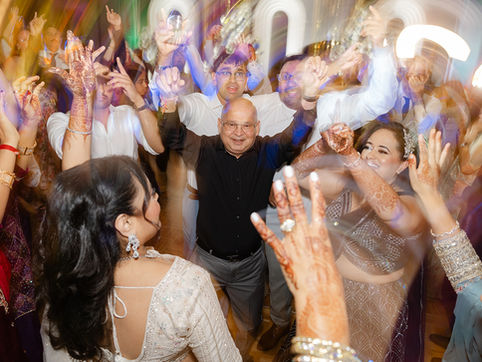 Candid photography of a wedding reception dance floor filled with joyful guests and hands raised in celebration during a vibrant party.