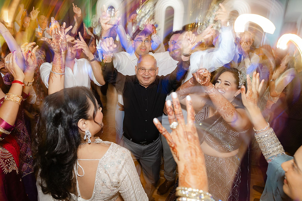A high-energy Indian wedding reception finale with the groom and guests dancing to Bollywood music under professional event lighting.