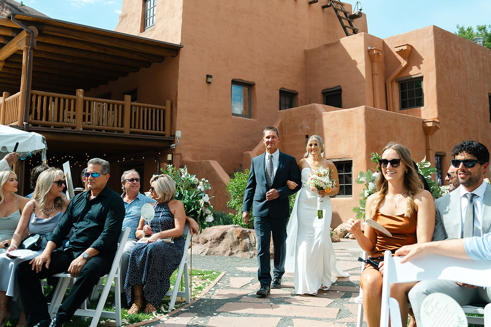 A bride in a white wedding gown walking down the aisle with her father during an outdoor Colorado Trading Post wedding ceremony.