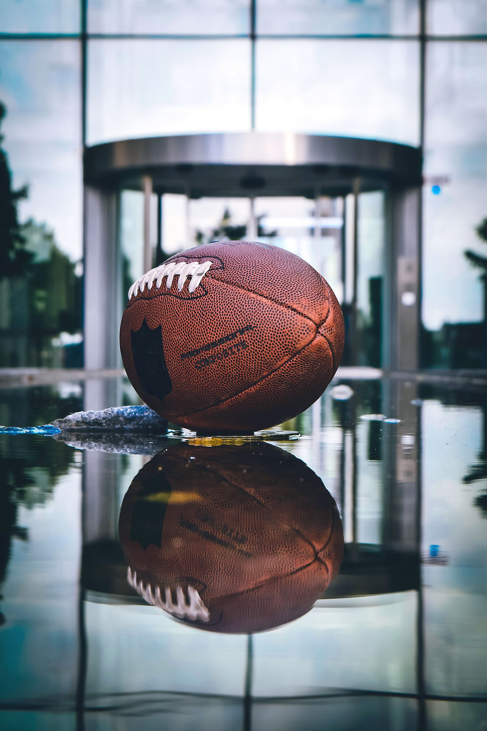 Closeup view of football laying on reflective surface with facility doors/building in the background.