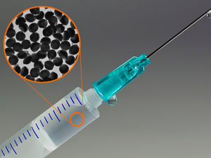 A syringe with a turquoise needle tip, liquid droplet, and close-up of black particles inside. Background is gray with blue markings.