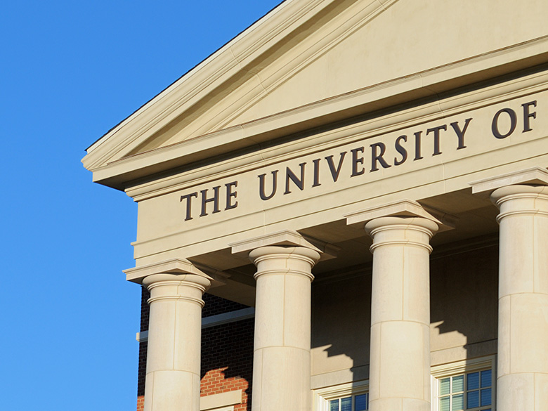 University building facade with tall columns and the sign THE UNIVERSITY OF against a clear blue sky