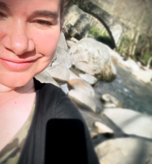 "Stefania Alba Nova smiling in front of a waterfall and stone bridge in the Smoky Mountains, founder of Flow Glow Mojo Dojo wellness brand."