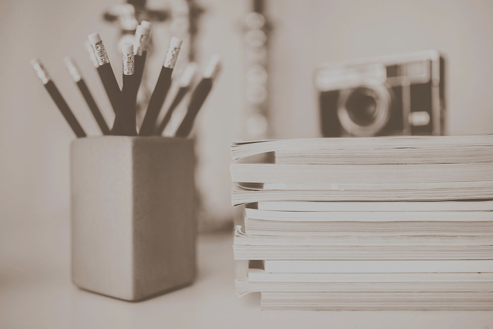 Picture of a cup of pencils on a desk next to a stack of paper with a camera sitting on top