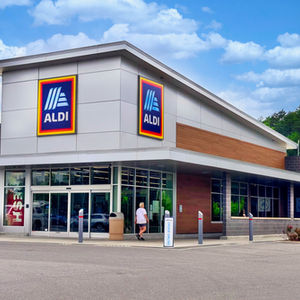 ALDI grocery store exterior with a person entering, blue sky overhead, and an ORDER ONLINE sign by the door.