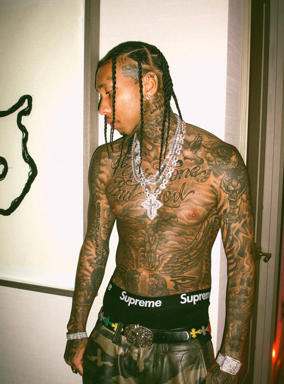Tyga shirtless in designer jewelry and Supreme boxers, showing tattoos while posing indoors, highlighting his success as one of the highest-earning musicians on OnlyFans.