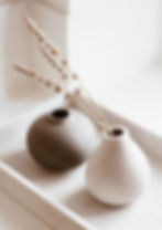 Two small vases with dried flowers, one gray and the other white, set against a bright, light-filled background, creating a peaceful and calm atmosphere.