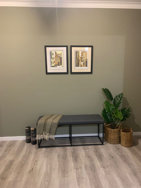 A green-painted wall with two paintings and a black display bench with two green plants. Living Services.