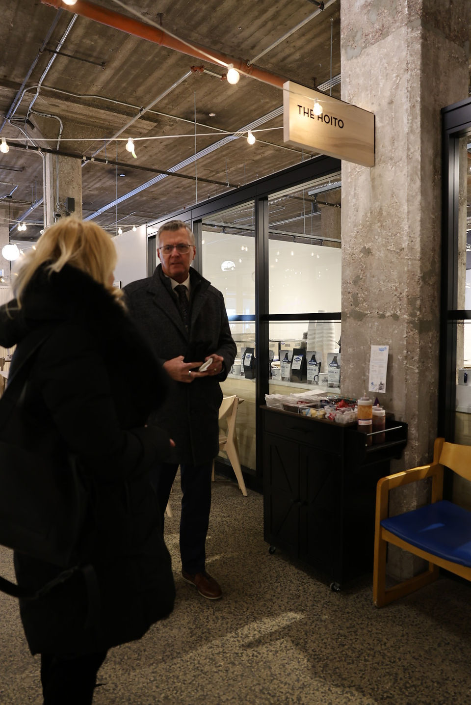 Man speaks to woman under "Volunteer" sign at an indoor event.