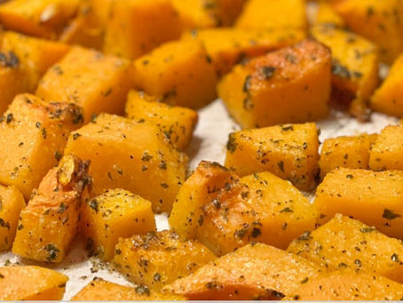 Cubes of squash covered in herbs on a baking sheet