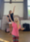 A young girl copying dance teacher, Miss Courtney's raised arm pose, demonstrating focused learning and movement imitation in a creative dance or ballet class at First Steps Performing Arts.