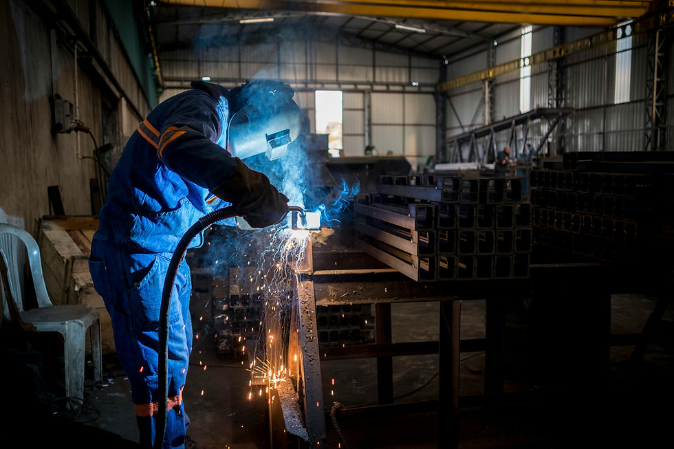Industrial welder working with protective gear, welding metal beams in a manufacturing workshop.