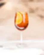 Photo of a Med Spritz in a large wine glass over ice, garnished with an orange slice, with a poolside background evoking a Mediterranean vibe.