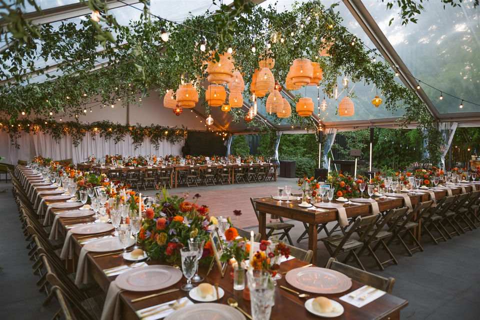 wedding tent decorated with fall colored floral arrangements, greenery, and lanterns.