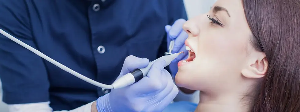 Dentist in blue uniform performing procedure on patient with visible teeth.