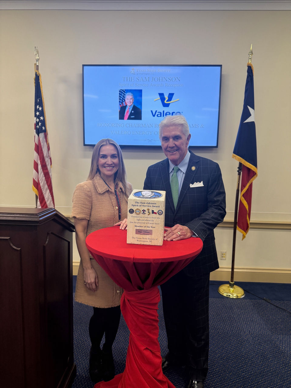 A woman and a man stand by a table with a white box at an event.