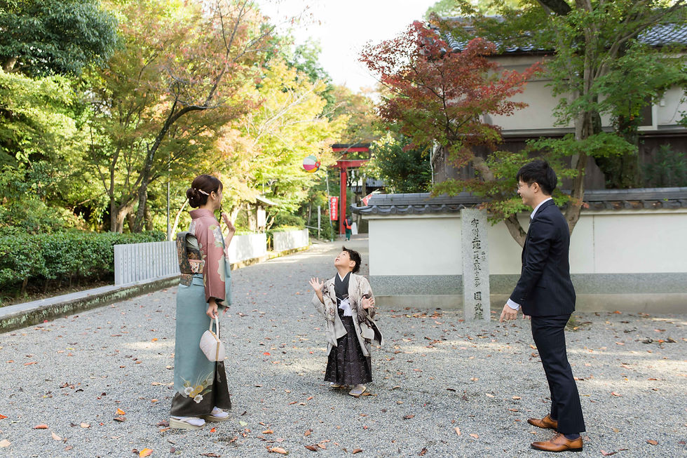 紅葉の神社境内で、着物の母と幼い子、スーツ姿の父が紙風船を見上げ、楽しそうに談笑している。