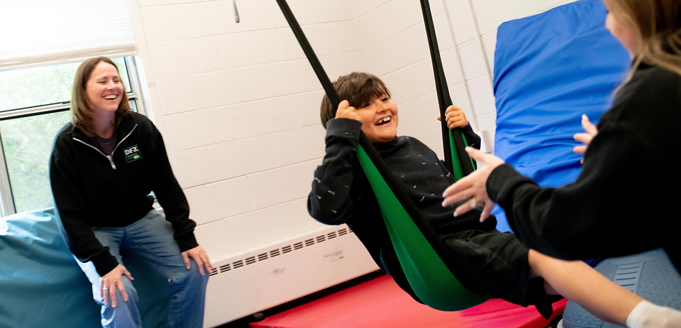 clinic scene with two therapists and boy in lycra swing.png