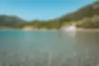 Белая церковь на песчаном пляже с прозрачной водой, зеленые холмы.