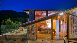 Современная вилла ночью с панорамными окнами, вид на спальню и горы.