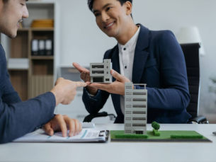 Two men looking at models of commercial properties while sitting at a desk.
