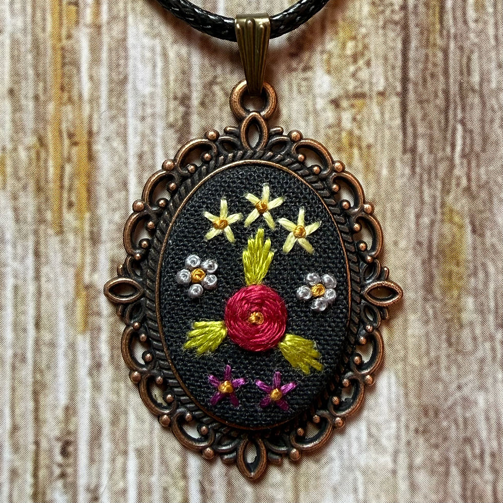 Thumbnail: Antique-style bronze oval necklace featuring hand embroidered floral design on black fabric.