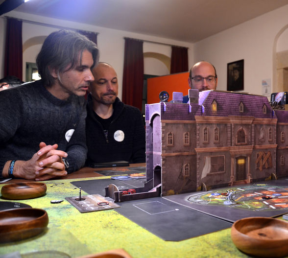 Drei Spieler spielen ein Brettspiel mit einem großen Gebäude