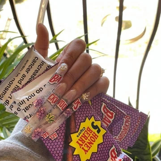 Hand holding Backwoods Honey Berry cigars pack and blunt wrap, showing popular flavored cigars in smoking culture
