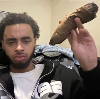 Person holding large blunt wrapped in tobacco leaf, demonstrating Backwoods-style rolling and smoking culture