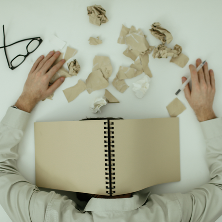 Man under a notebook with papers shreded in front of him, feeling overwhelmed